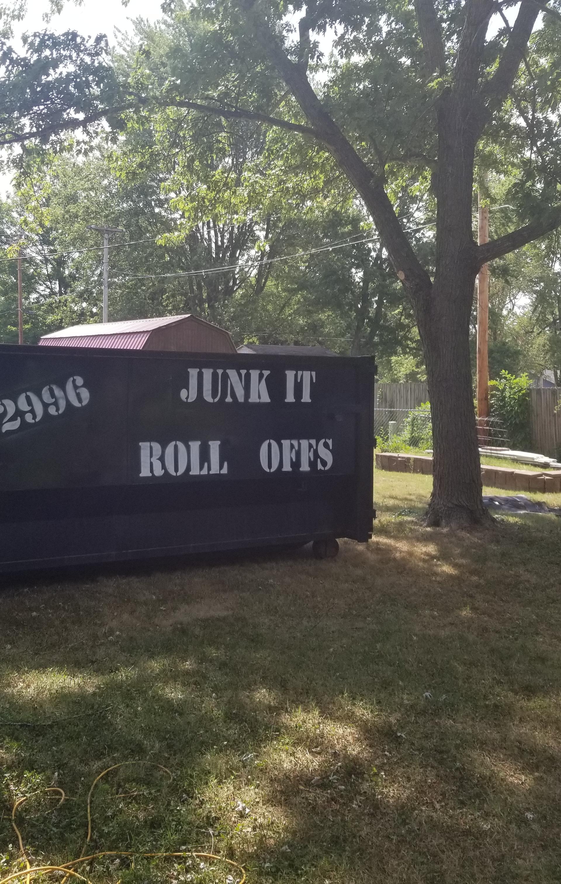 Black 25-yard roll-off dumpster from Junk It Roll Offs placed in a residential backyard in Fordland, MO, with roofing shingles nearby.