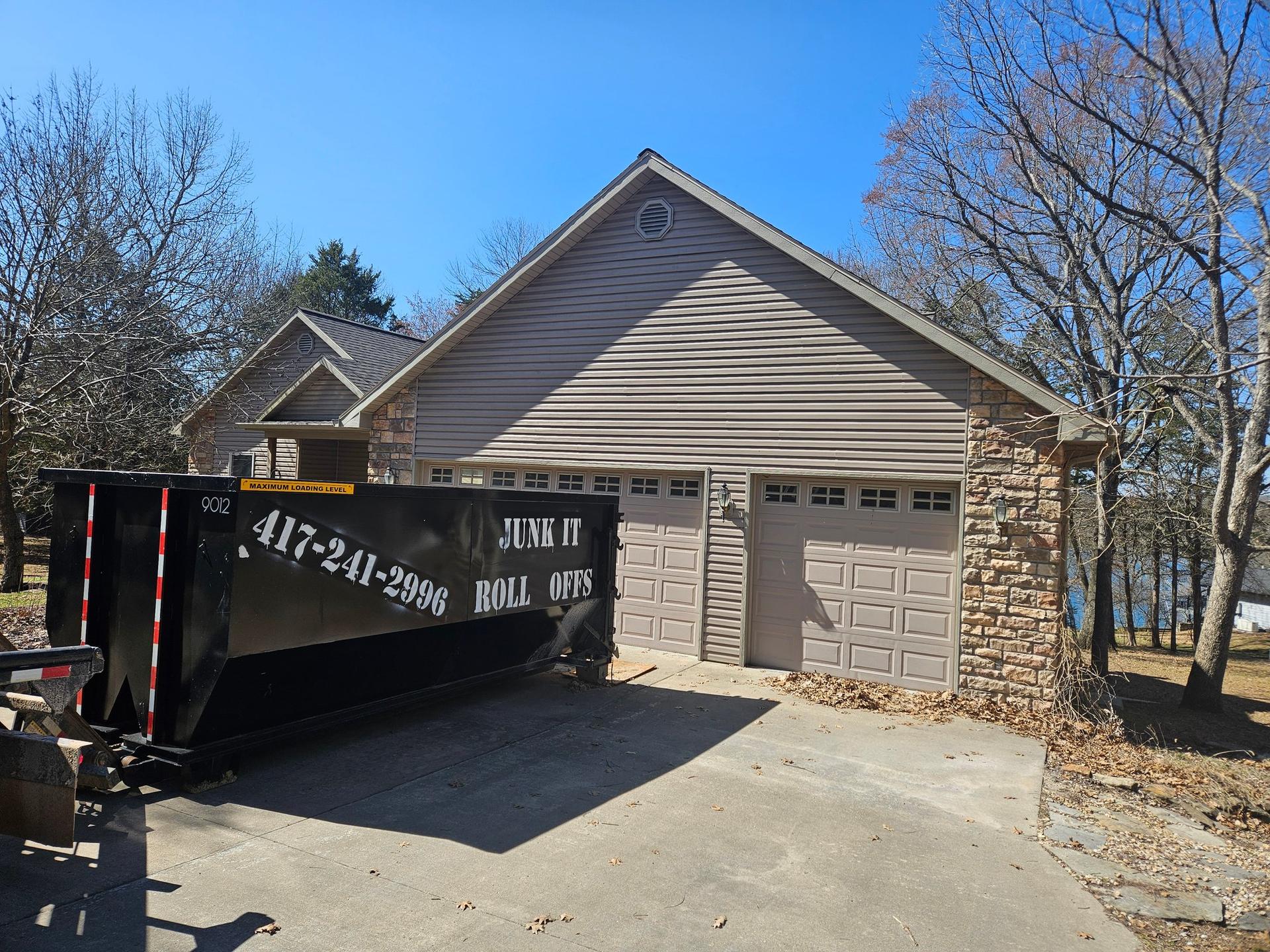 Black 25-yard Junk It Roll Offs dumpster on a residential driveway in Hartville, Missouri, for a home cleanout project.